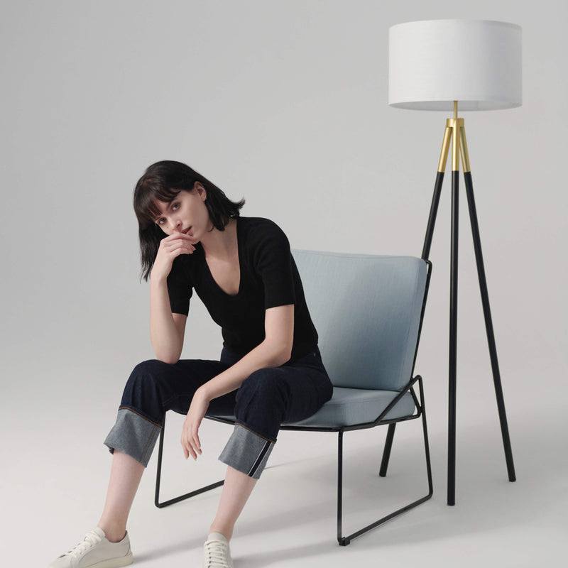 Young woman sitting on a modern chair next to a stylish floor lamp in a minimalist room.