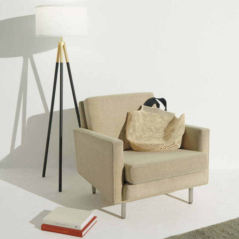 Stylish beige armchair with woven bag next to modern floor lamp in contemporary living room.