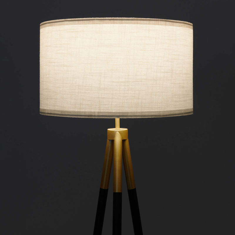 Modern tripod floor lamp with beige fabric shade on dark background.