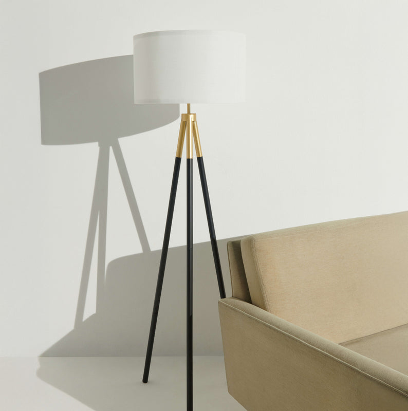 Modern black tripod floor lamp with a white shade next to a beige sofa in a minimalist living room.