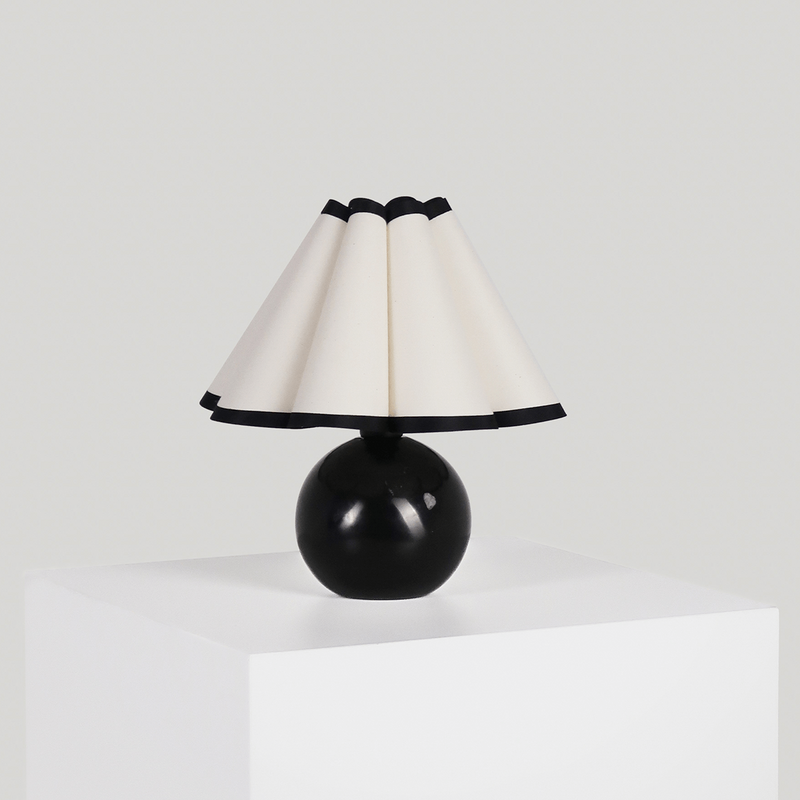 Black modern table lamp with cone-shaped shade on a white pedestal.
