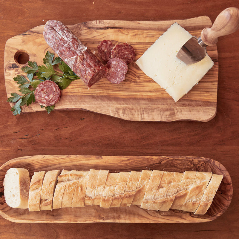 Rustic charcuterie board with sliced salami, cheese wedge, and crusty bread on wooden platters.