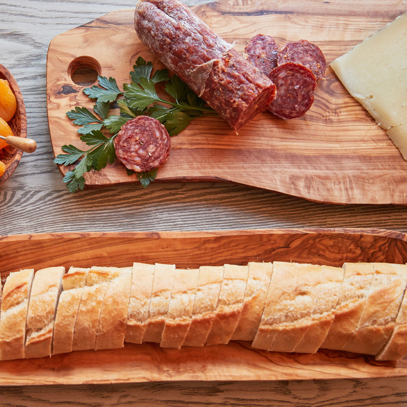 Assorted charcuterie board with sliced salami, cheese, and baguette on wooden platter.