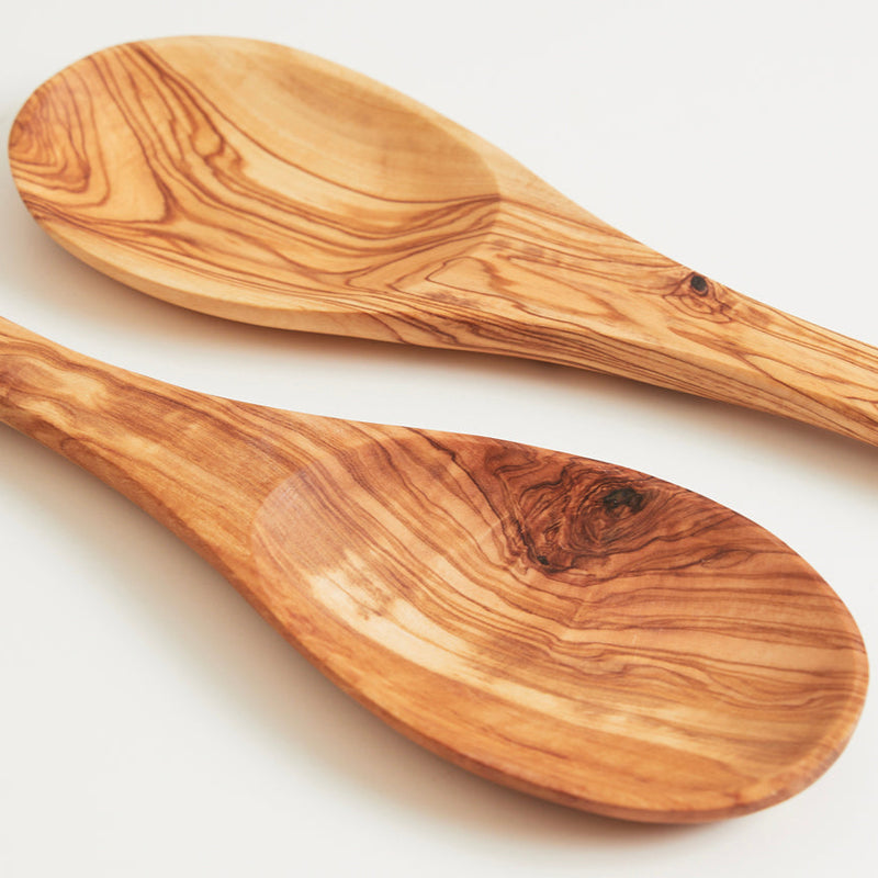 Handcrafted olive wood cooking spoons with natural grain patterns on a white background.