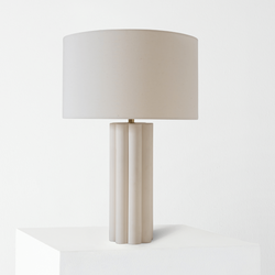 Modern beige table lamp with a cylindrical base and drum shade on a white pedestal.