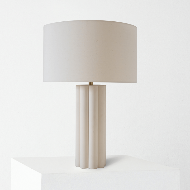 Modern beige table lamp with a cylindrical base and drum shade on a white pedestal.
