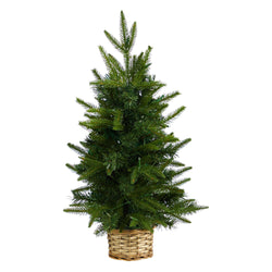 Small artificial tabletop Christmas tree in a woven wicker basket with lush green pine branches, holiday home decor