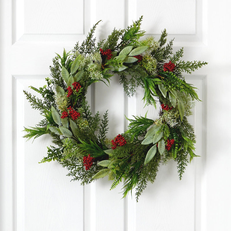 Christmas wreath of mixed evergreen cedar and eucalyptus with red berry clusters hanging on a white paneled front door