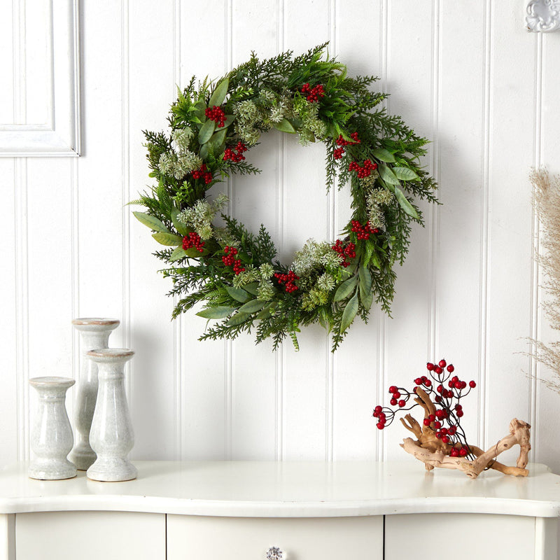 Indoor Christmas wreath of mixed evergreens and red berries on a white paneled wall above a white console table with ceramic candlesticks, farmhouse holiday decor