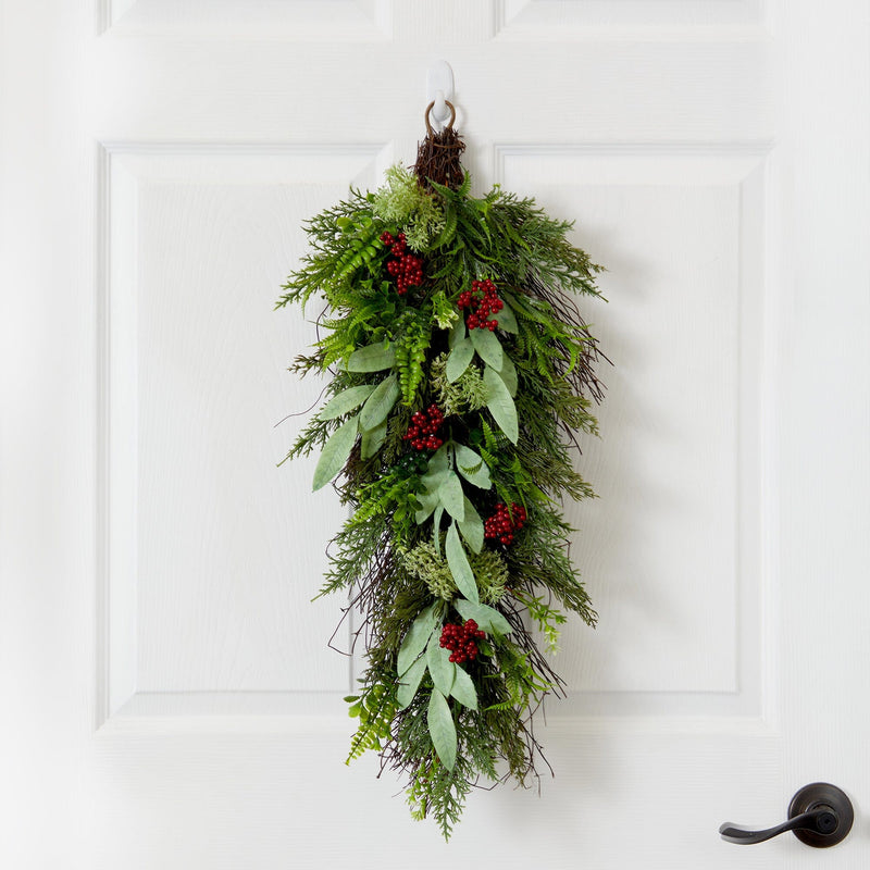 Vertical evergreen and eucalyptus door swag with red berry clusters hanging on white front door — rustic Christmas holiday decoration