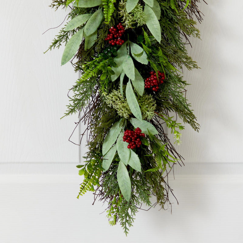 Evergreen holiday door swag with eucalyptus leaves, cedar and fern sprigs and red berries on white wood background
