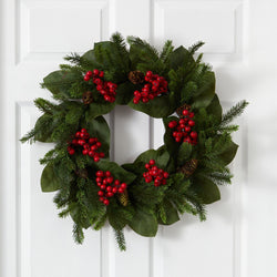 Christmas wreath with evergreen branches, magnolia leaves, red berries, and pine cones hanging on a white front door