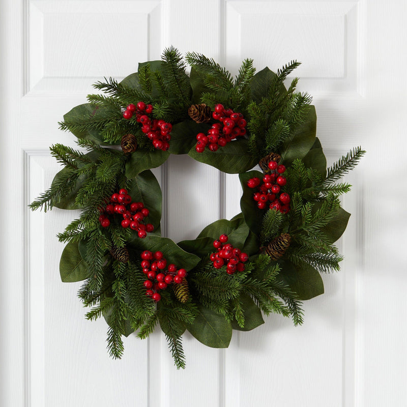 Christmas wreath with evergreen branches, magnolia leaves, red berries, and pine cones hanging on a white front door