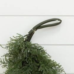 Cedar evergreen swag tied to a green plastic hanger on white shiplap wall — rustic holiday front-door decor