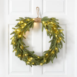 Green pine Christmas wreath with warm white LED lights and jute hanger on white front door, holiday door decoration