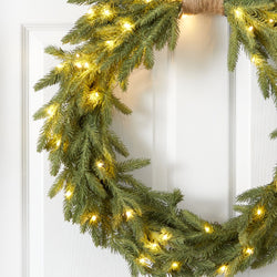 Green pine Christmas wreath with warm white LED string lights hanging on a white paneled front door, festive holiday decor
