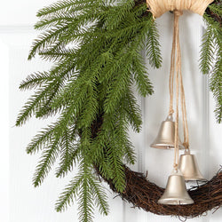 Christmas wreath with evergreen branches and three gold bells on a grapevine base hanging on a white front door