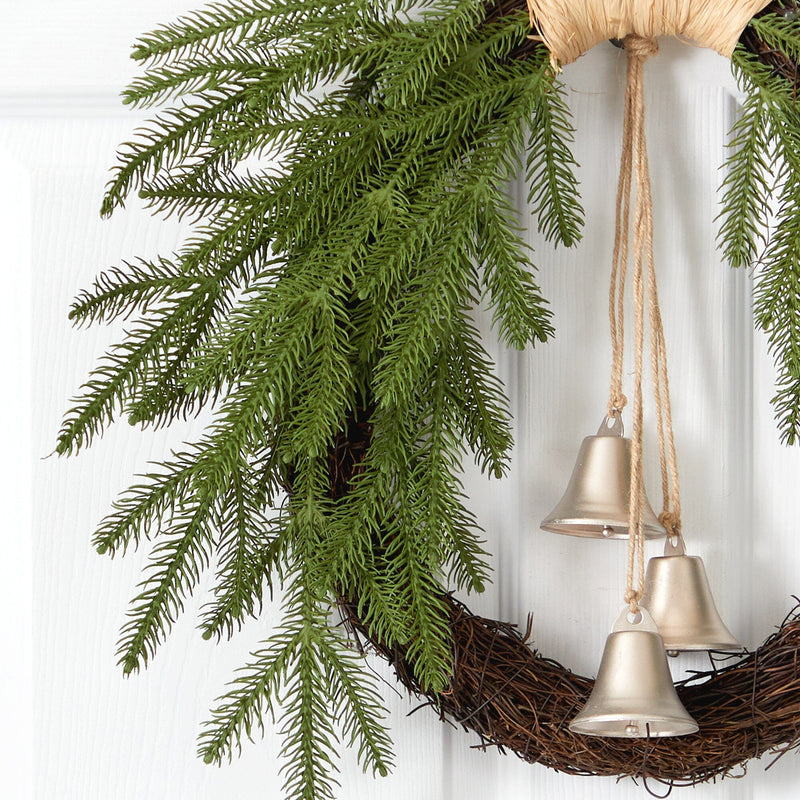 Christmas wreath with evergreen branches and three gold bells on a grapevine base hanging on a white front door
