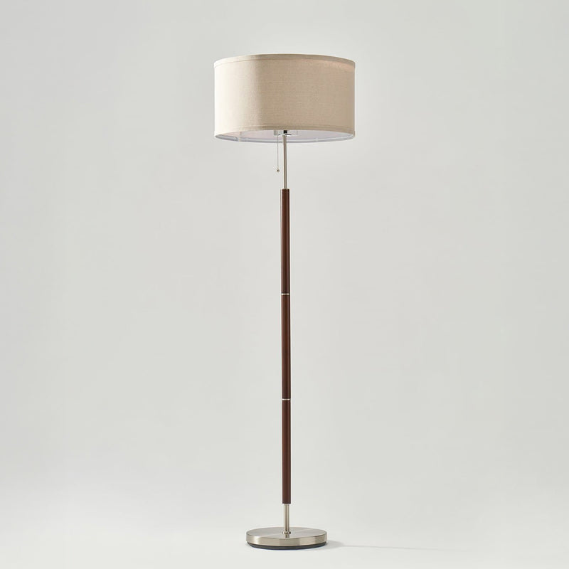 Contemporary floor lamp with beige linen drum shade, dark wood segmented pole, brushed nickel accents and round metal base with pull-chain switch, modern living room lighting