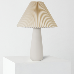 Minimalist beige pleated lampshade on matte white ceramic table lamp, modern neutral bedside decor