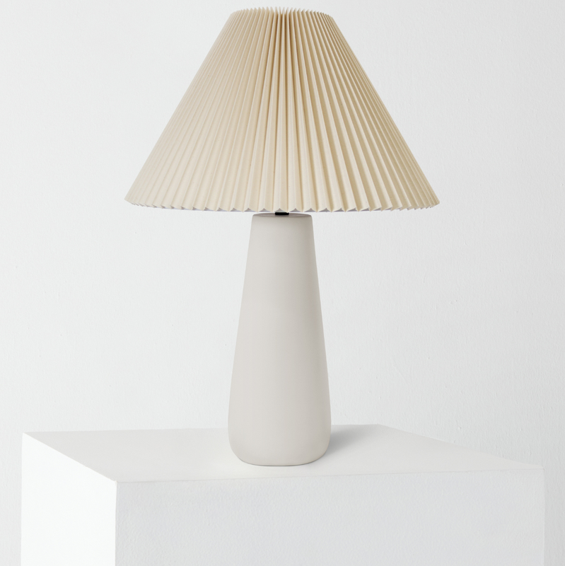 Minimalist beige pleated lampshade on matte white ceramic table lamp, modern neutral bedside decor