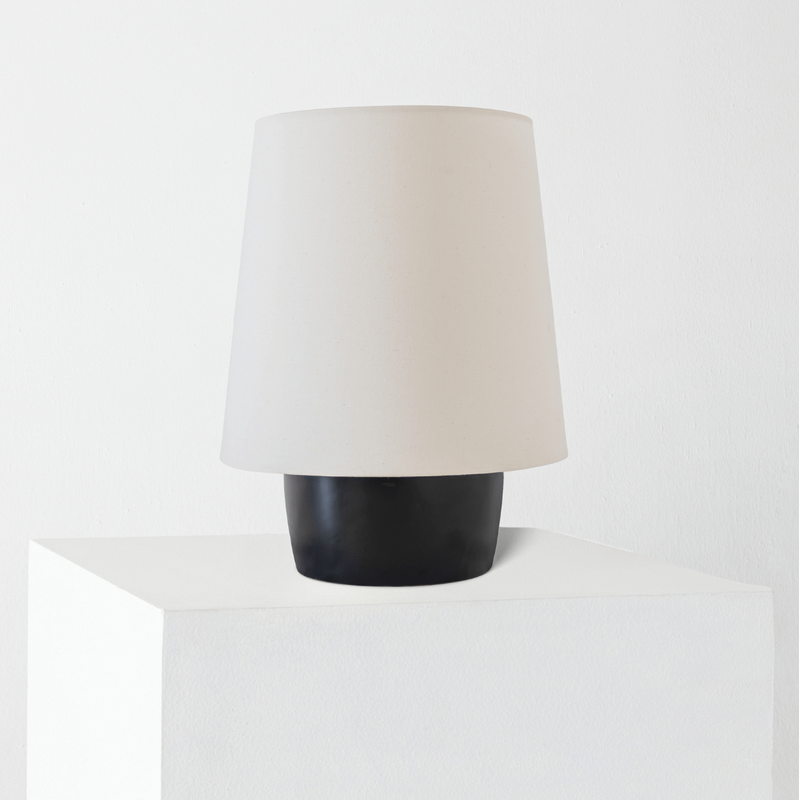 Minimalist modern table lamp with white fabric shade and matte black ceramic base on white pedestal, home decor lighting.