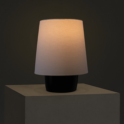 Modern minimalist table lamp with beige fabric shade and black ceramic base casting warm ambient light