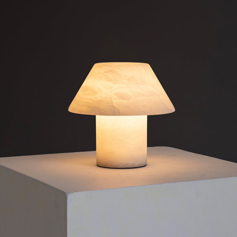 Modern mushroom-shaped white table lamp emitting warm ambient light on a minimalist white pedestal against a dark background