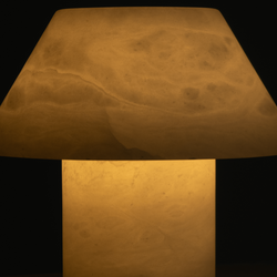 Modern mushroom-shaped alabaster table lamp emitting warm amber glow, minimalist bedside lamp for cozy ambient lighting