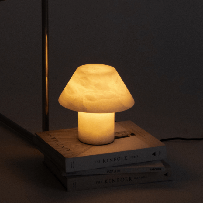 Minimalist modern metal-framed chair beside warm mushroom-shaped table lamp on stacked Kinfolk books in dim living room