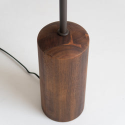 Minimalist walnut wood cylindrical lamp base with matte metal stem and black cord on white background