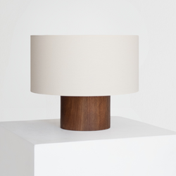 Minimalist modern table lamp with cylindrical walnut wood base and cream fabric drum shade on white pedestal, ideal mid-century modern bedside or living room lighting