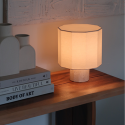 Modern minimalist table lamp with octagonal linen shade and textured ceramic base on wooden console table with stacked books and neutral vases, warm ambient lighting