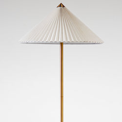 Minimalist modern brass floor lamp with white pleated conical lampshade on plain white background