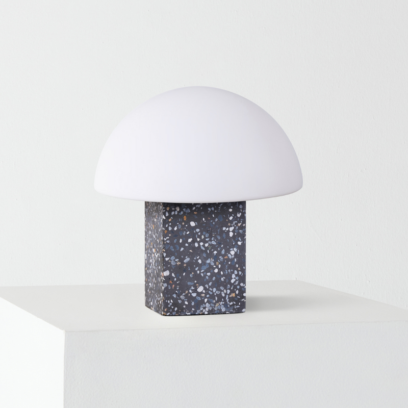 Modern minimalist mushroom table lamp with white dome shade and dark terrazzo block base on white pedestal