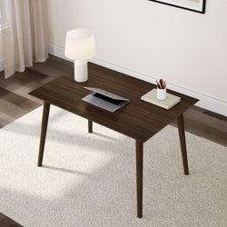 Minimalist home office with a dark wooden desk, laptop, lamp, and stationary on a light carpet.