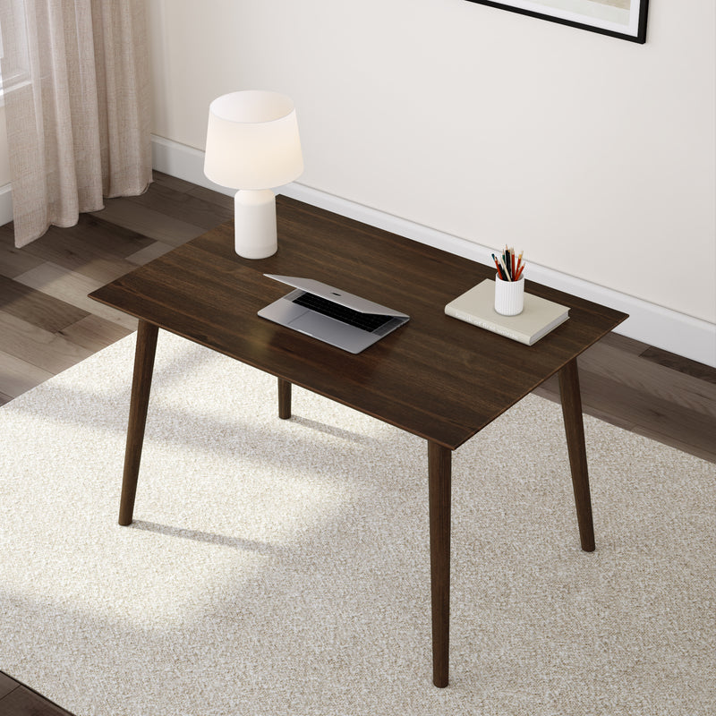 Minimalist home office with a dark wooden desk, laptop, lamp, and stationary on a light carpet.