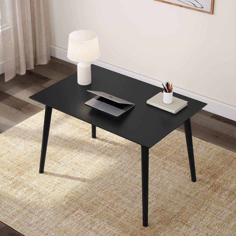 Modern black desk with a laptop, lamp, and stationery on a beige rug in a minimalist home office setting.