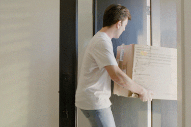 Man in white shirt carrying cardboard box into modern home entryway.