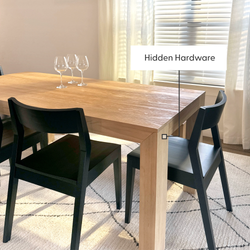 Modern dining table with hidden hardware and sleek black chairs in sunlit room.