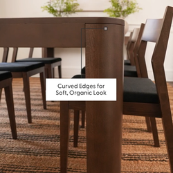 Wooden dining table with curved edges and chair set on woven rug, ideal for a modern and organic interior design.