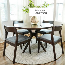 Solid wood dining set with round table and four chairs on patterned rug in bright dining room.