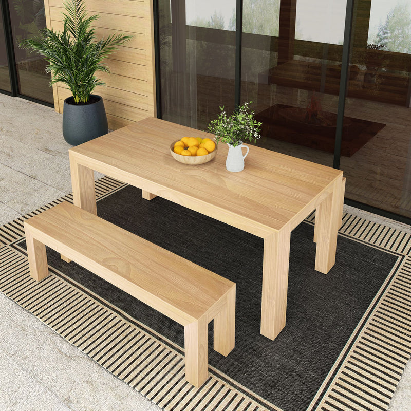 Outdoor wooden dining table and bench set with a bowl of lemons and a plant, placed on a decorative rug near a glass window.