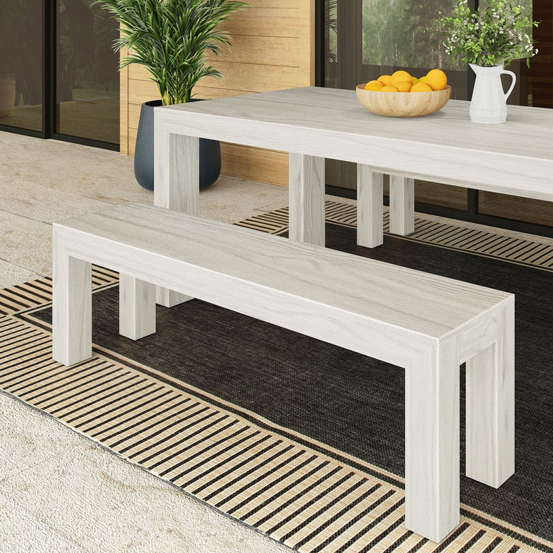 Modern minimalist outdoor dining set with light wood table and bench on a striped rug, accented by a potted plant and decorative bowl.