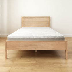 Minimalist beige wooden bed frame with a comfortable memory foam mattress in a bright bedroom.