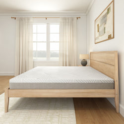 Modern bedroom interior with a minimalist wooden bed frame and comfortable mattress, natural light streaming through sheer curtains.