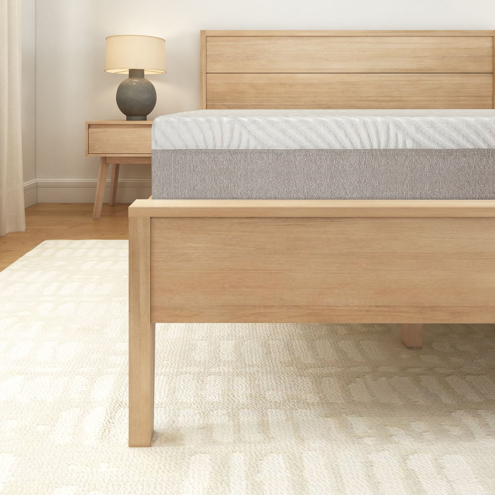 Modern wooden bed frame with mattress in a minimalist bedroom setting featuring a bedside table and lamp.