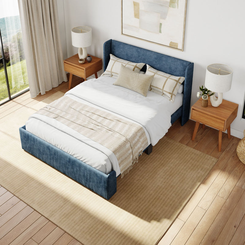 Modern bedroom with blue upholstered bed frame, beige pillows, wooden nightstands, and natural light.