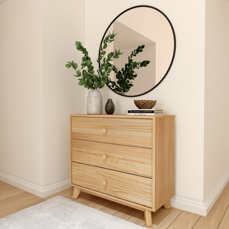 Natural wood dresser with three drawers, round mirror, and green plant in modern minimalist bedroom.