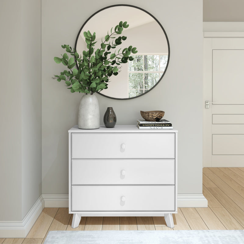 White dresser with a round mirror and decorative plants in a modern minimalist hallway.